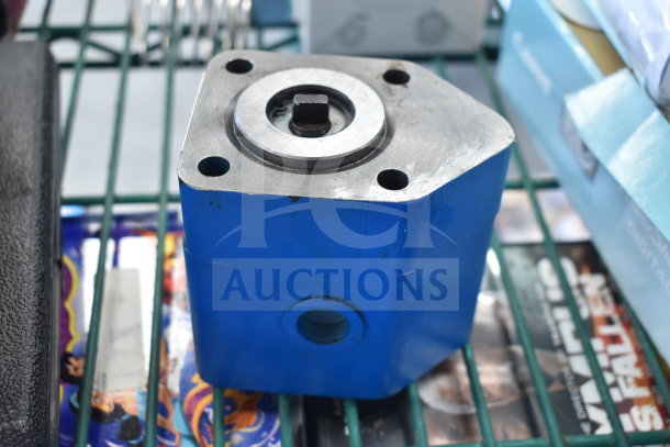 Blue metal component, possibly part of the Fryclone Oil Pump 259POFM728L, shown on a metal rack. Features drilled holes and a central shaft.