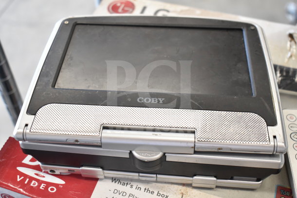 Coby portable DVD player in used condition on top of LG DVD player box. Visible wear on casing.