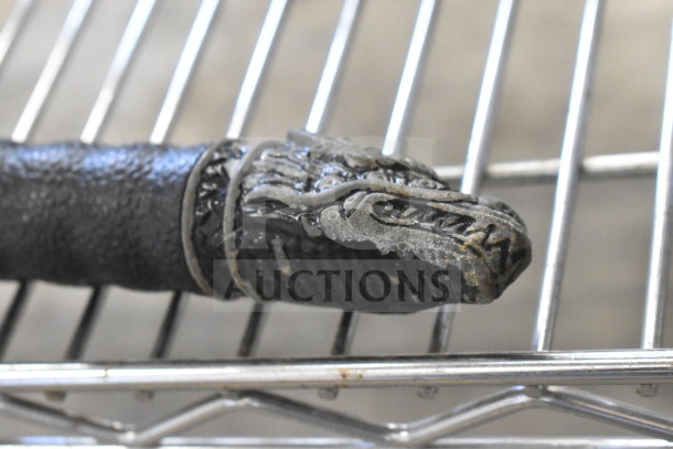 Samurai sword with intricate dragon design on sheath cap, textured black handle, displayed on metal rack.