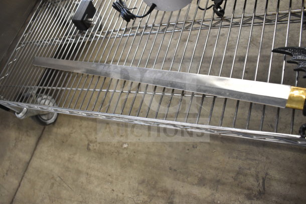 Samurai sword with gold hilt, displayed unsheathed on a metal rack. Silver blade, polished finish, excellent condition.