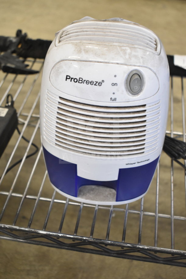 ProBreeze dehumidifier on metal shelf; white with dirt marks; features "on" and "full" indicators; Whisper Technology label.