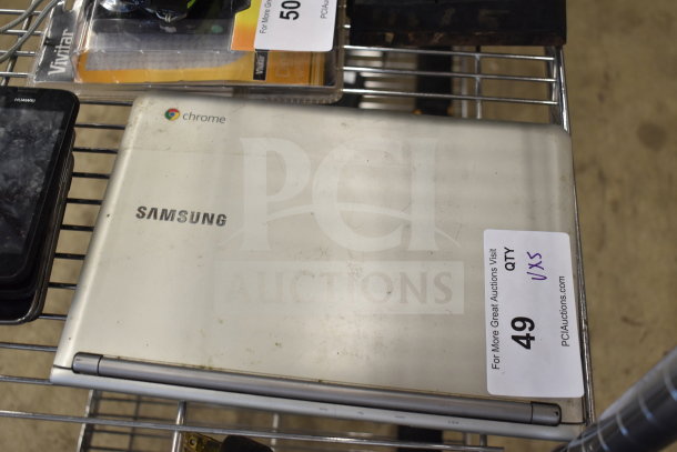 Samsung Chrome laptop and four smartphones, including Huawei, on auction. Visible wear on laptop. Auction label with quantity details.