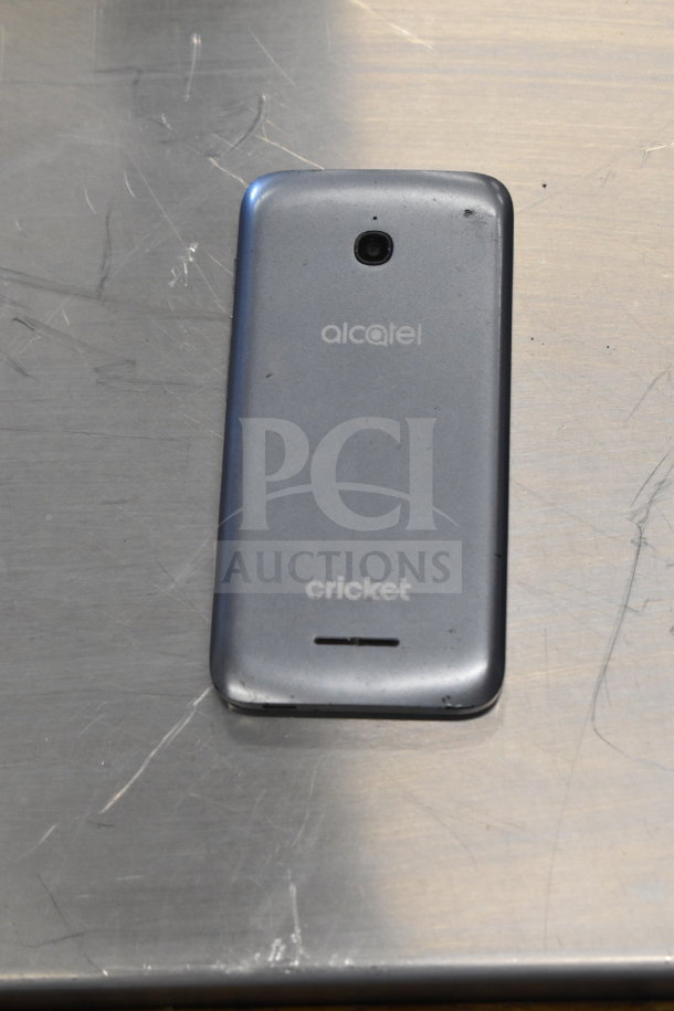 Alcatel smartphone with minor wear, marked "cricket," part of an auction lot with Samsung laptop and 4 smart phones.
