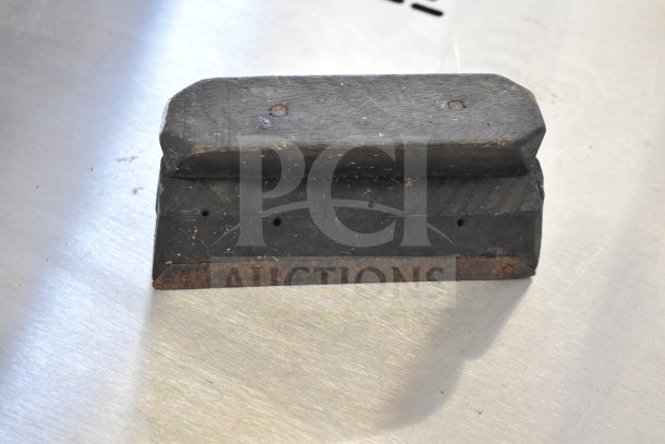 A small, rectangular, weathered wooden block with metal screws and a rusted base, showing signs of age and wear.