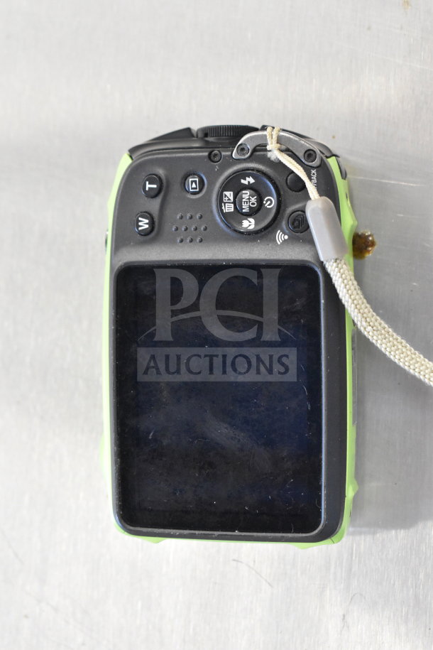 Digital camera with a scuffed LCD screen, buttons for zoom and menu, and an attached wrist strap, part of an 8-item auction lot.
