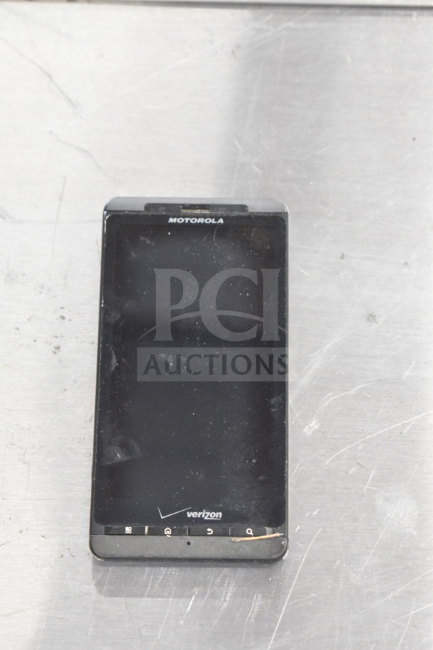 Motorola smartphone, Verizon branding, black color, visible wear on screen, part of a lot of 8 items including iPods.