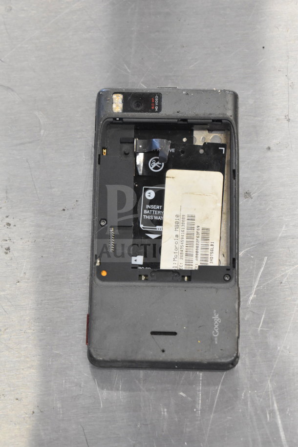 Smartphone with missing battery cover, visible internal components, and Motorola branding on battery inside. Used condition.