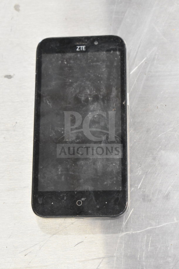 ZTE smartphone with visible wear on screen, part of auction lot including three smartphones and Genesis Ultimate Portable Game Player.