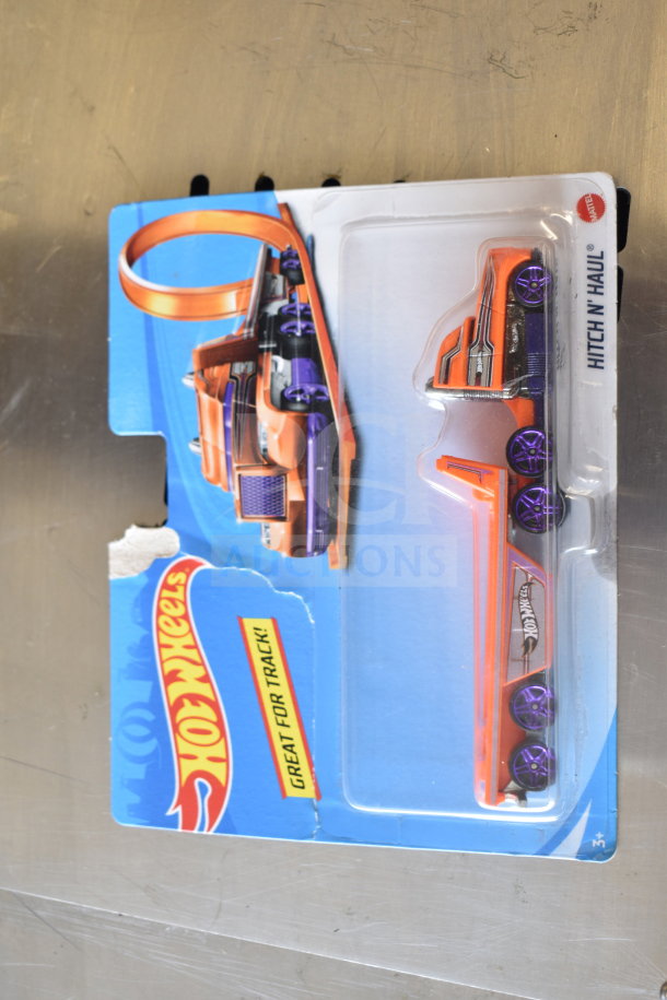 Hot Wheels car in packaging with orange and purple design. Packaging shows wear. Labeled "Hitch N' Haul."