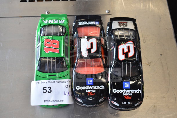 Three die-cast cars, one green with number 18, two black with Goodwrench Service Plus branding, on a metallic surface.