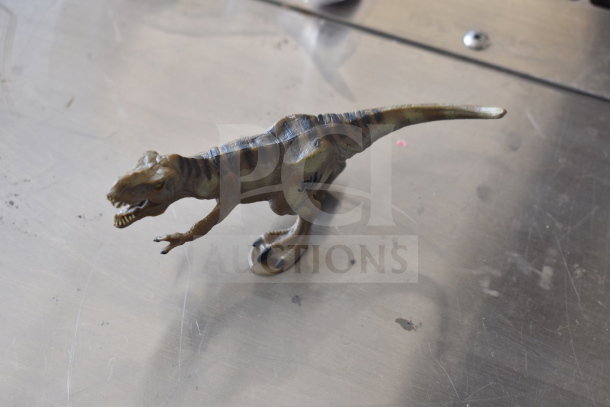 Dinosaur figurine on metal surface, part of a 15-item mixed auction lot with toys and collectibles.