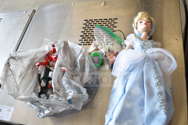 Assorted items including a Cinderella doll, Tamagotchi, Strawberry Shortcake figurines, dinosaur toy, and hand sanitizer cozies.