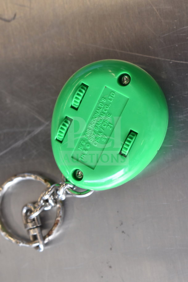 Green keychain toy with McDonald's branding, 1997 Bandai Co., Ltd., China. Includes metal keyring. Appears in good condition.