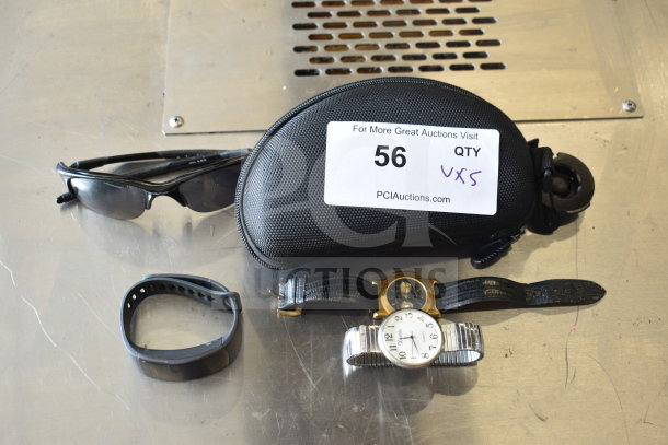 5 assorted items: sunglasses, black case, fitness watch, two analog watches. Auction label "56 QTY VXS" visible.