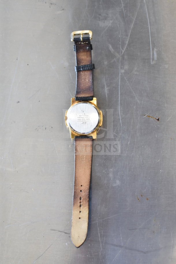 Wristwatch with gold-tone case, scratched back, leather strap; markings "JAZ" and "USA 19R". Condition shows wear.