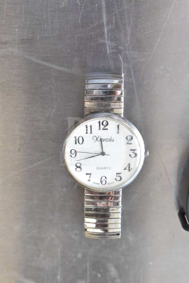 Xanadu quartz watch with silver expandable band, white dial, black numerals. Slightly worn condition, Japan movement.