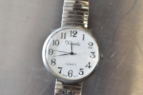 Xanadu quartz watch with silver expandable band. White dial, black numerals. "Japan Movt" marked. Vintage condition.