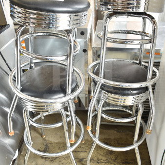 Four chrome finish stools with black cushioned seats, featuring a sleek retro design. Slight wear visible on chrome legs.