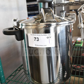 Brand new Monix Pressure Pot, stainless steel, visible scratch and dent, with secure lid and black handles. Auction tag labeled "73".