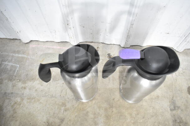 Lot of kitchen items including two stainless steel air pots with labeled lids, colander, stock pot, and China cap strainer.