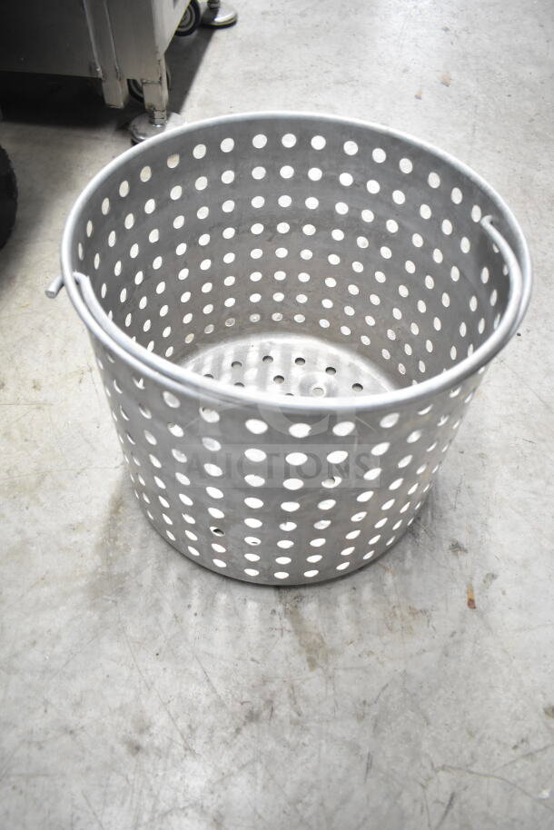 Aluminum colander with perforated sides on concrete floor, part of a kitchenware auction lot.