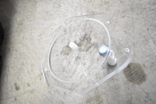 Acrylic lid or component with a small blue-capped knob and white nozzle on a concrete surface, part of assorted kitchen tools lot.