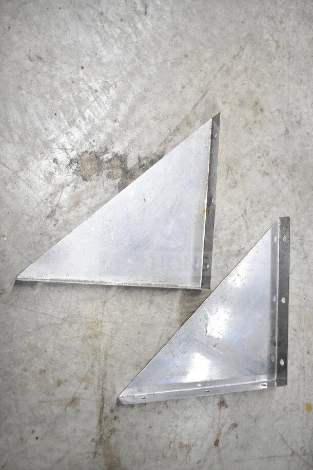 Metal brackets on a concrete surface, showing some signs of wear and rust, likely part of an auction lot.