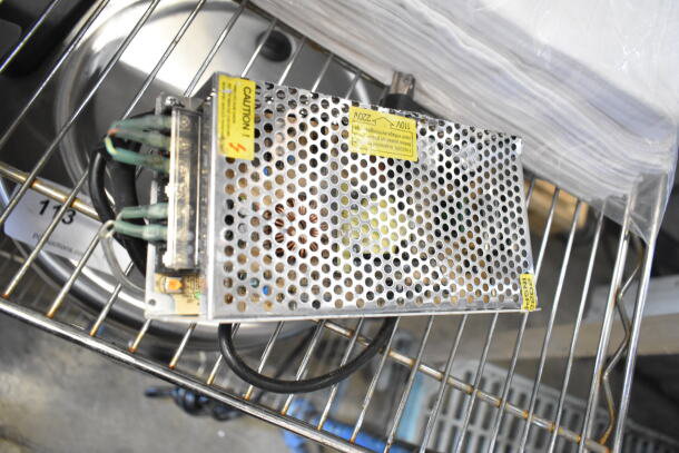 Metal appliance or electronic device with wiring on metal rack, caution labels visible. Includes faucet kit, drop-in bin, and towels.