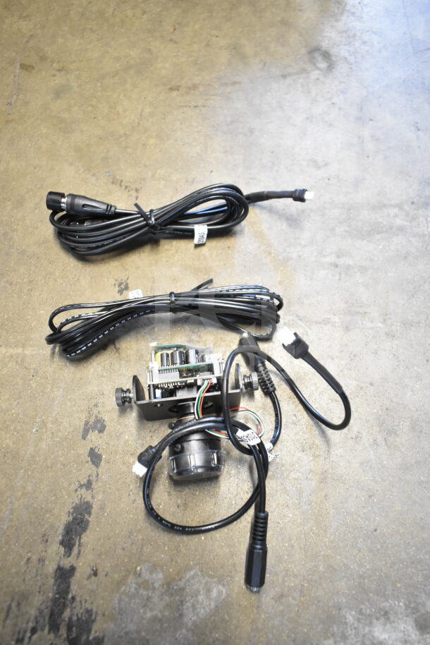 Three items including a Wren camera with intricate wiring and a SVW PTZ adapter, plus two coiled black cables on a concrete surface.