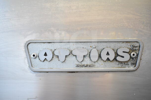 Attias rotisserie oven tag showing brand and "Made in USA" marking, on stainless steel surface.