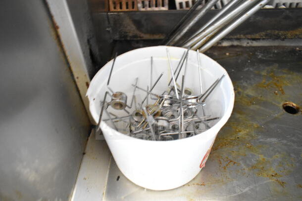 Bucket of metal skewers belonging to an Attias gas-powered rotisserie oven, indicating commercial use.