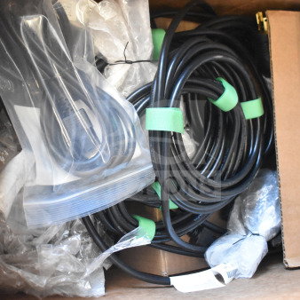 A box of wires, including coiled black cables with green ties, some in plastic bags. Condition appears unused.