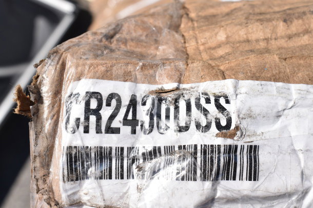 Damaged cardboard box with label "CR2430DSS" and a barcode, part of a scratch and dent auction lot.