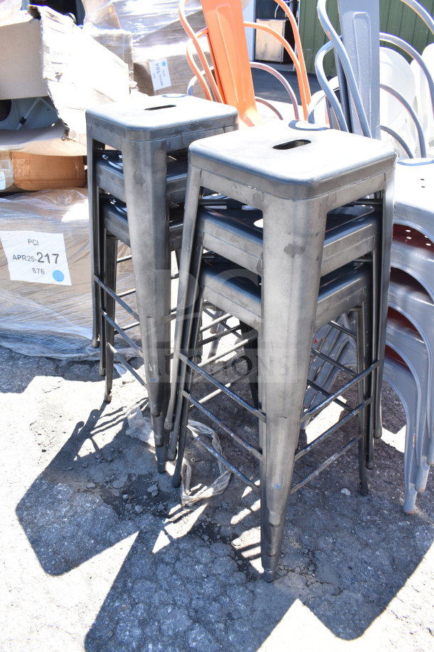 Stacked gray Tolix style bar stools, brand new with minor scratches. Includes orange chairs and white patio chairs nearby.