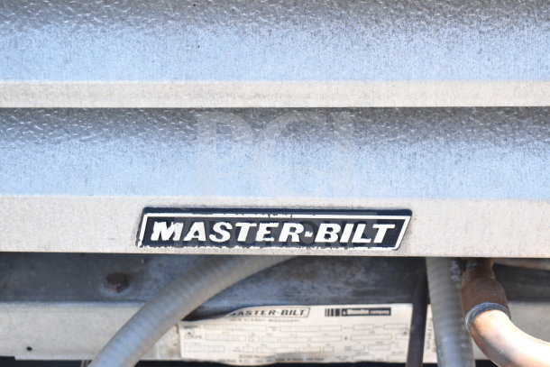 Master-Bilt logo on equipment, metallic surface, pipes below. Used for identification of the 8'x12' walk-in box with compressor.