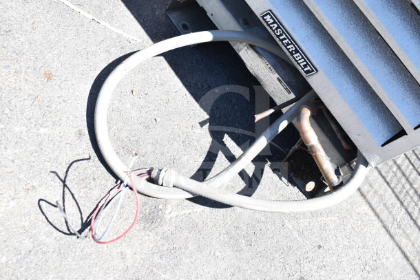Master-Bilt compressor unit with label, showing copper pipes and electrical wires on concrete surface.