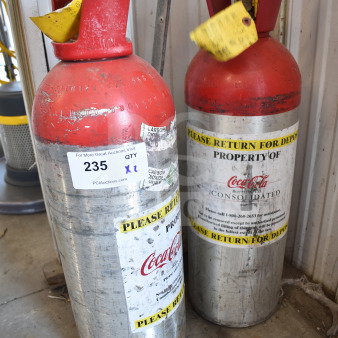 Two metal CO2 tanks labeled "Property of Coca-Cola," with red tops and deposit return stickers. Buyer pickup required.