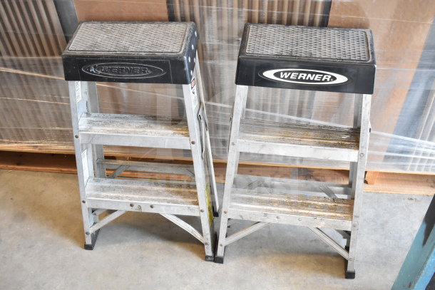 Two Werner aluminum step ladders with anti-slip treads. Visible wear. Branded top caps. Set of four in auction.