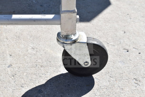 Close-up of a commercial caster from a pan transport rack. The caster is metal with a black rubber wheel, showing slight wear.