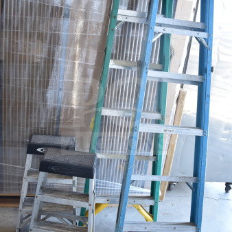 Four various ladders, including step stools and extension ladders, in used condition. Mixed colors and types.