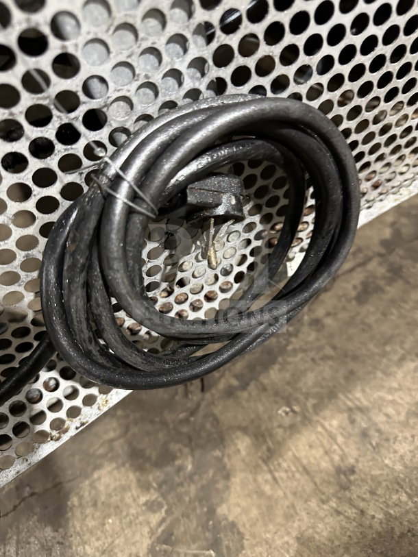 Coiled power cord against perforated metal backdrop, related to True TWT48D4 refrigerator unit.
