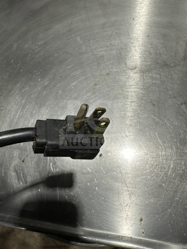 Close-up of a three-prong electrical plug against a stainless steel surface; part of a Beverage-Air refrigerated chef base.
