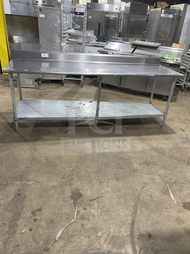 L&J stainless steel worktop table with undershelf, on legs. Durable commercial design, clean surface, ideal for kitchens.