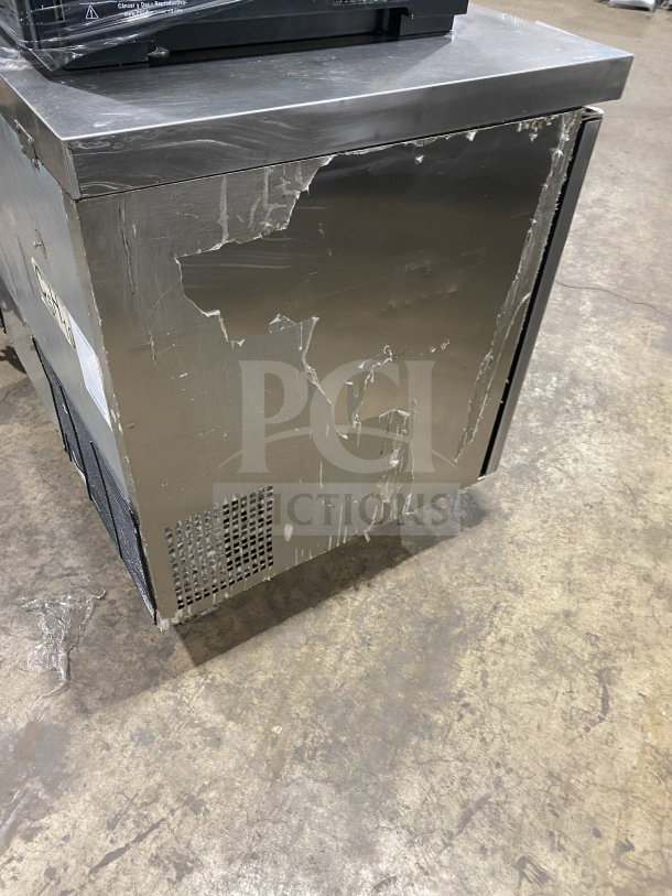 Migali stainless steel 2-door undercounter refrigerator, Model CU60RHC, on casters with visible wear.