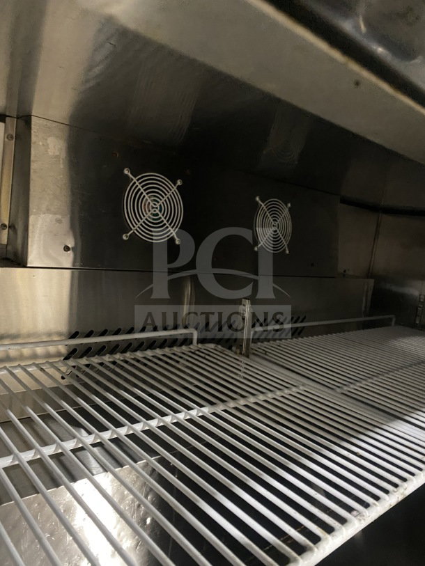 Migali CU60RHC stainless steel 2-door undercounter refrigerator with poly-coated wired rack, fans visible, on casters.