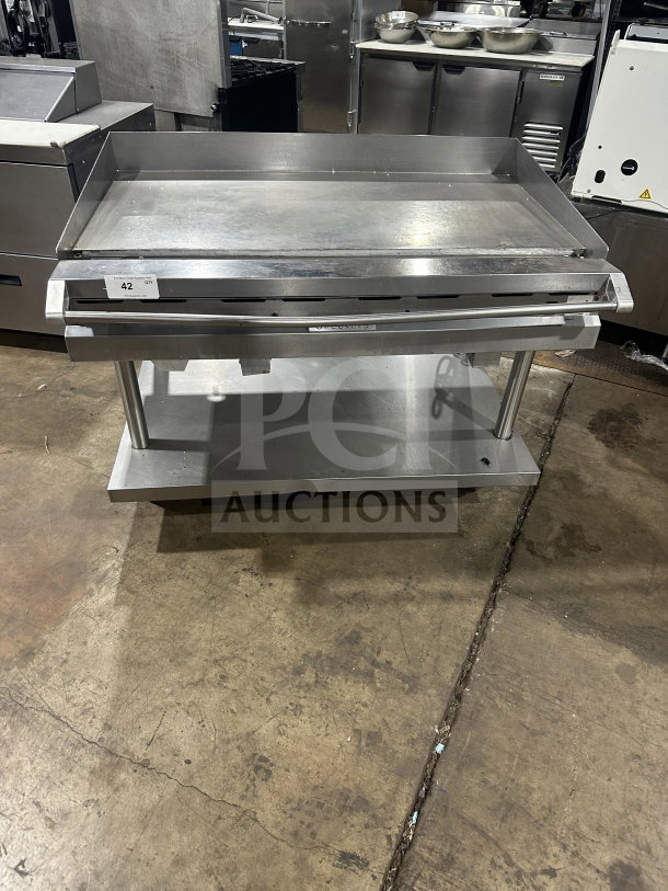 Commercial stainless steel griddle with cheese melter and overfire broiler on casters, item 42, in used condition.