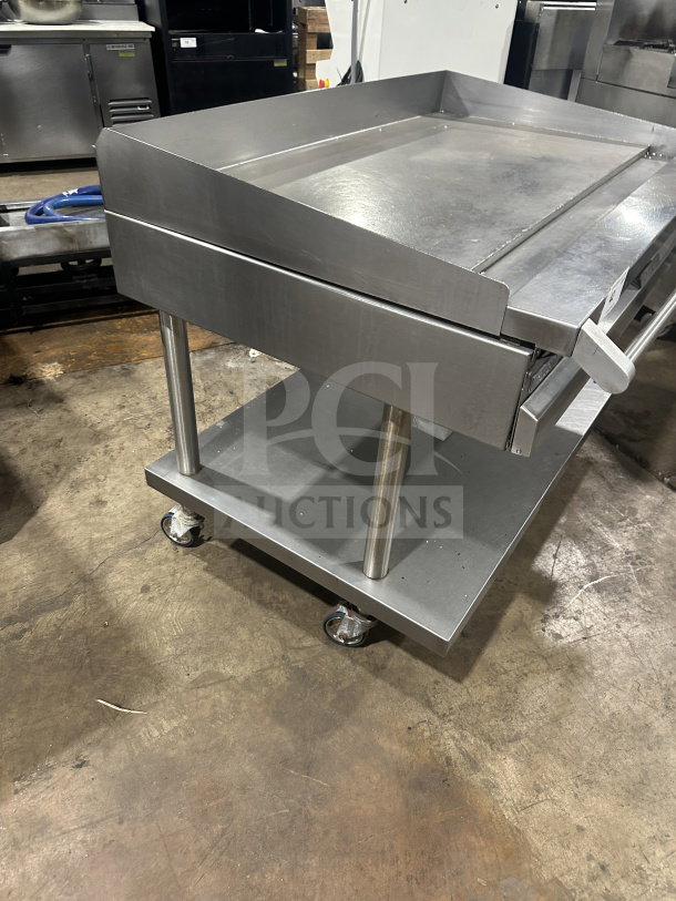 Commercial stainless steel griddle with cheese melter and overfire broiler, in good condition, mounted on casters for mobility.