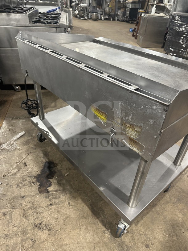 Commercial stainless steel griddle and cheese melter with overfire broiler on casters. Features visible wear and power cord.
