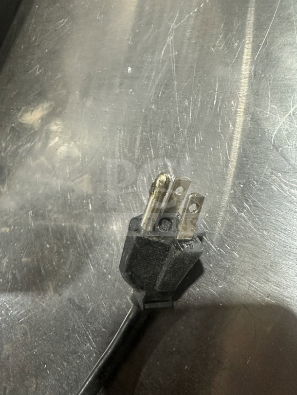Close-up view of a three-prong electrical plug for the Crathco CS-2E/1D-16 beverage dispenser, resting on a stainless steel surface.