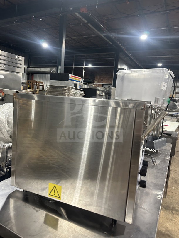 Belleco JT2H stainless steel conveyor toaster, electric-powered, countertop model, warning label visible, in warehouse.
